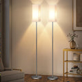 Minimalist standing floor lamp with fabric drum shade beside a sofa in a living room