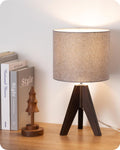 Wooden tripod table lamp with fabric shade glowing on a bedroom nightstand