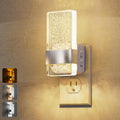 Sconce style plug in night light glowing warmly in a hallway wall outlet at night