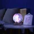 Galaxy-print moon lamp glowing on a table beside a photo frame