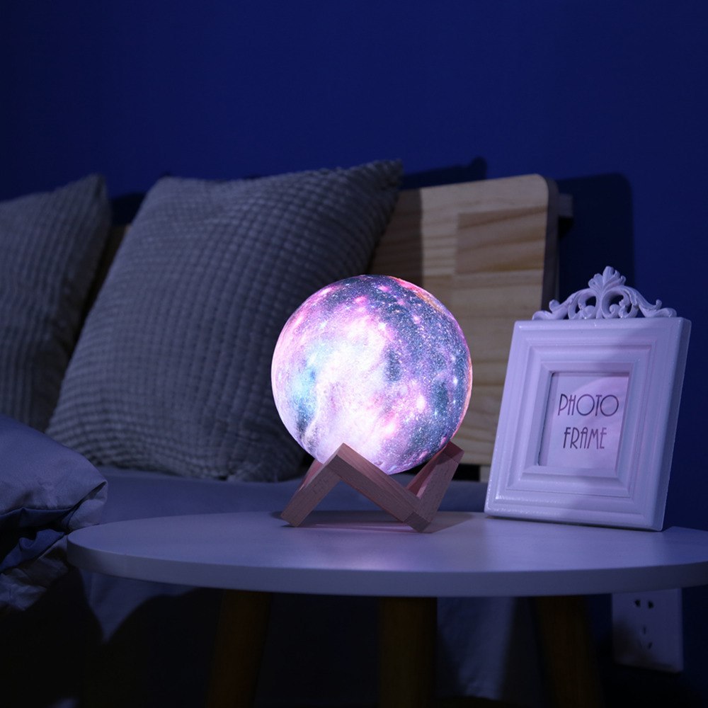 Galaxy-print moon lamp glowing on a table beside a photo frame
