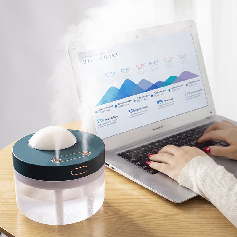 Dark green rotating humidifier releasing mist beside a laptop on a desk