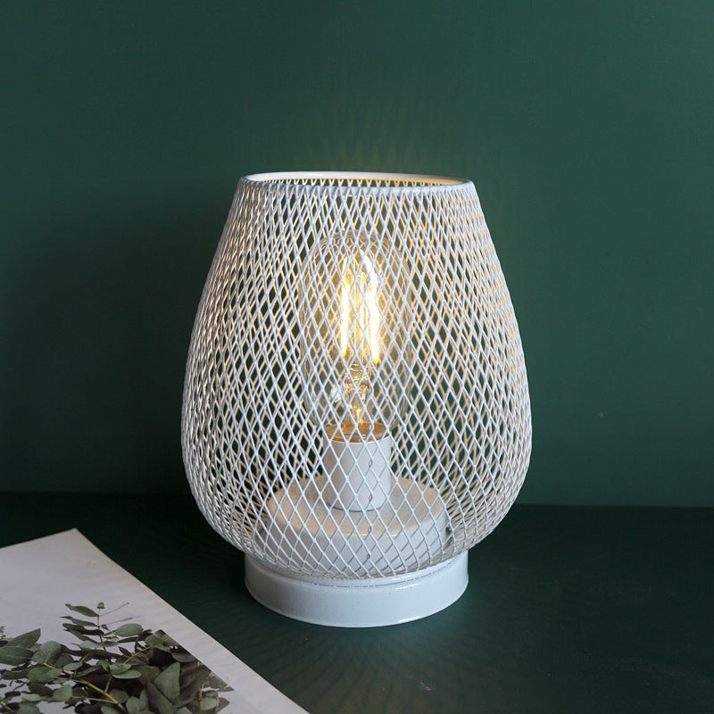 White wire mesh birdcage lamp lit against a dark green wall