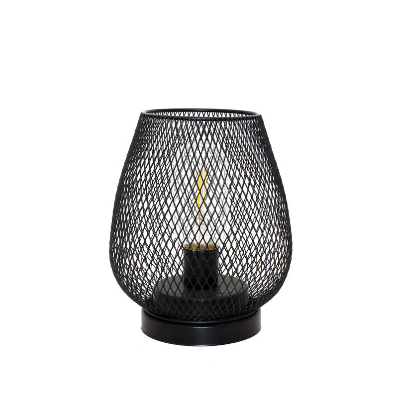 Black wire mesh birdcage table lamp with a filament bulb, plain background