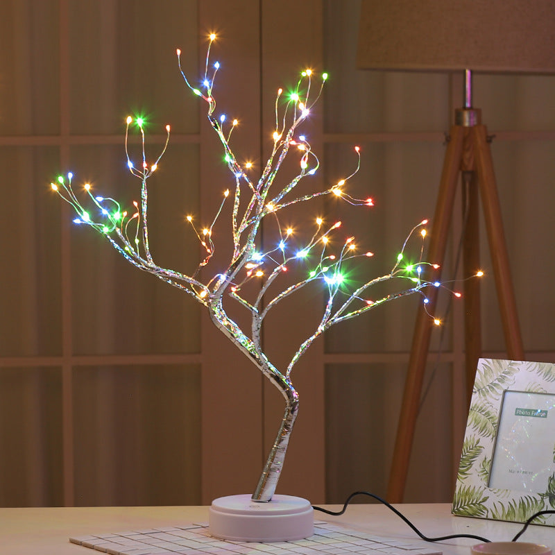 LED bonsai branch tree light in multicolour mode on a desk beside a lamp