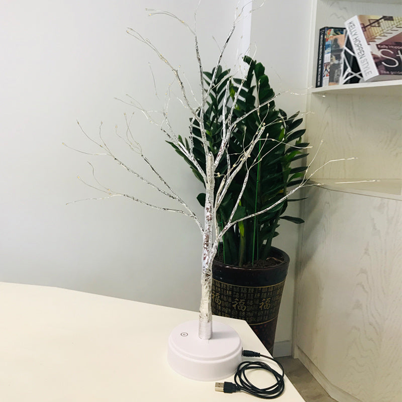 LED bonsai branch tree light on a desk next to a plant, USB cable visible