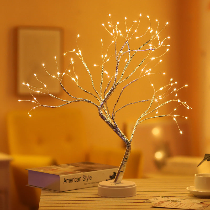 LED bonsai branch tree light lit warm on a side table beside books