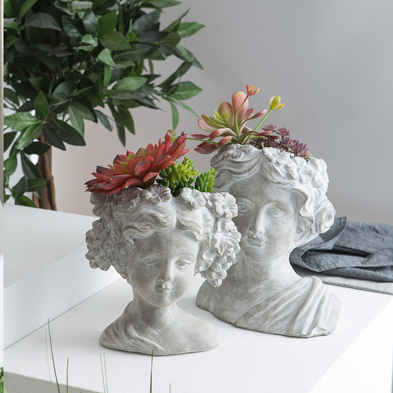 Two cement bust planters on a white shelf, each planted with succulents