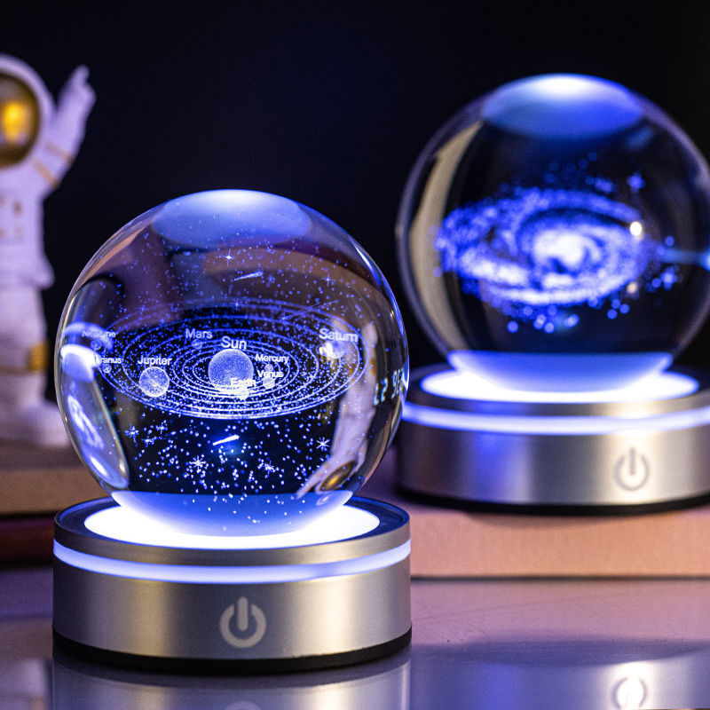 Two crystal ball night lights engraved with the solar system and a galaxy, lit blue
