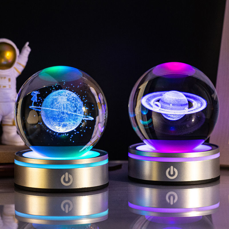 Two crystal ball night lights engraved with a planet and Saturn, lit blue and purple