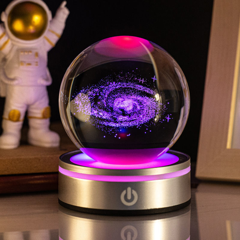 Galaxy crystal ball night light on a pink-lit base beside an astronaut figurine