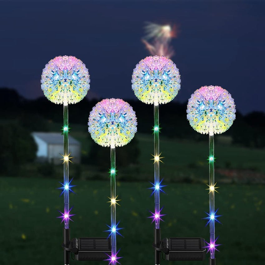Four dandelion solar lights lit across a lawn at night with a house behind