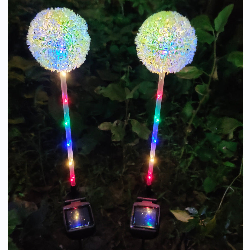 Two dandelion solar lights close up at night, stems lit in rainbow colours