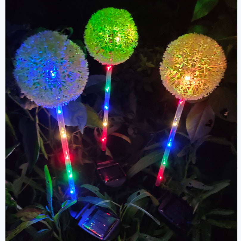 Three dandelion solar lights in green, blue and amber among plants at night