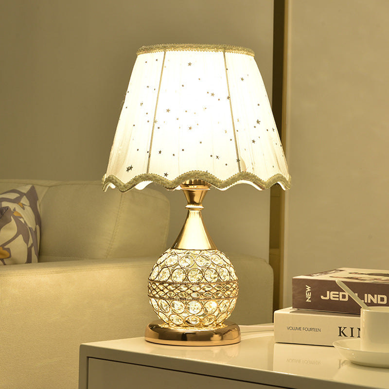 Gold crystal table lamp with a pleated fabric shade lit beside books