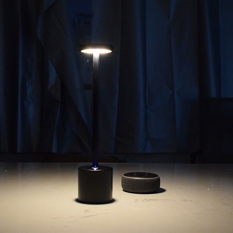 Black cordless table lamp lit in a dark room next to its charging base