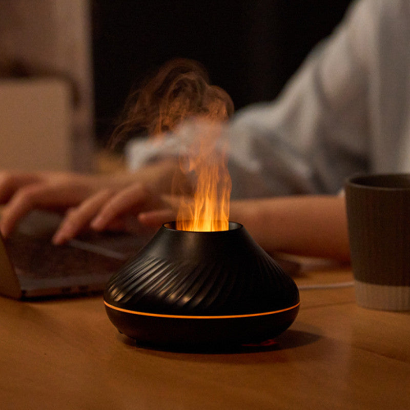 Black flame aroma diffuser releasing lit mist on a desk beside a person typing