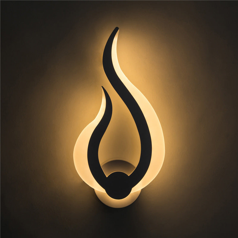 Flame-shaped LED wall sconce lit on a dark wall, warm light spreading upward