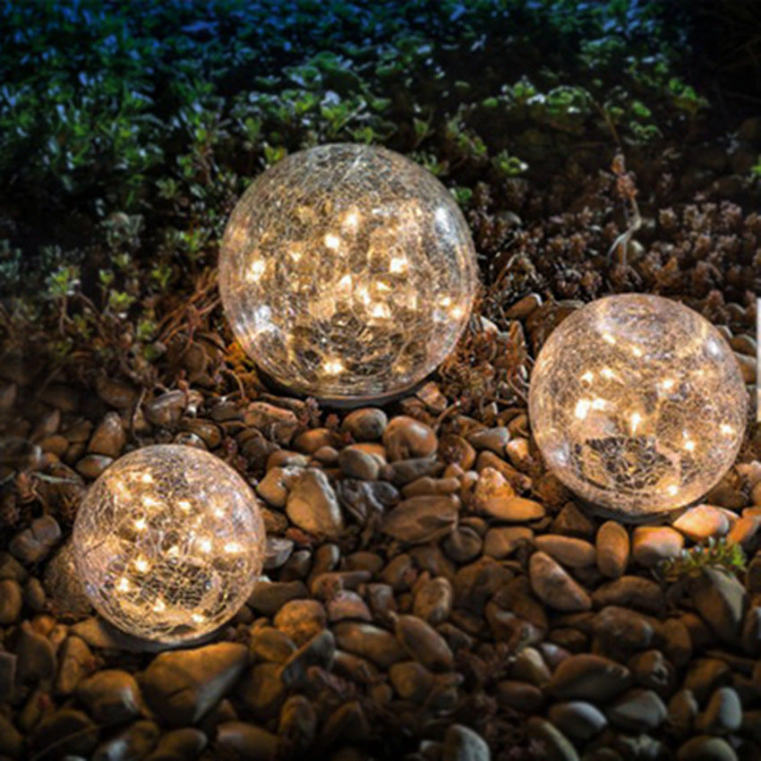 Three crackle-glass solar ball lights glowing warm among garden pebbles