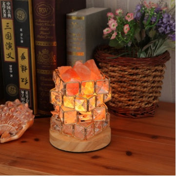 Salt crystal lamp lit warm on a wooden shelf beside books and a basket