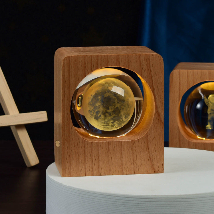 Crystal ball with a moon engraving lit amber inside a square wooden frame