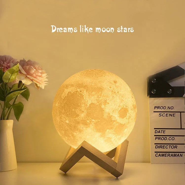 3D moon table lamp glowing warm on a wooden stand beside roses