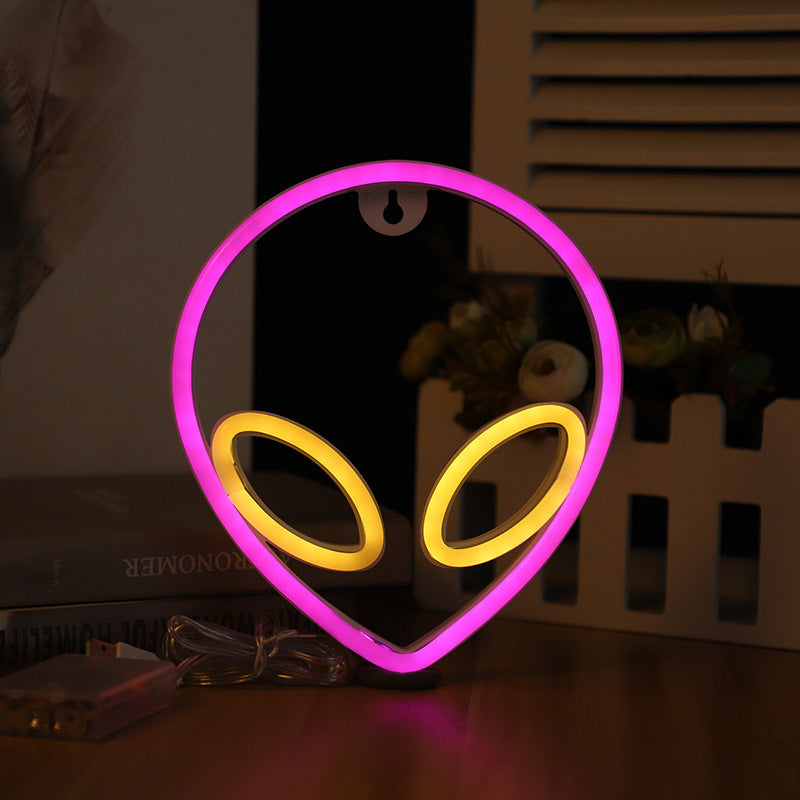Alien head neon wall sign lit in pink with yellow eyes
