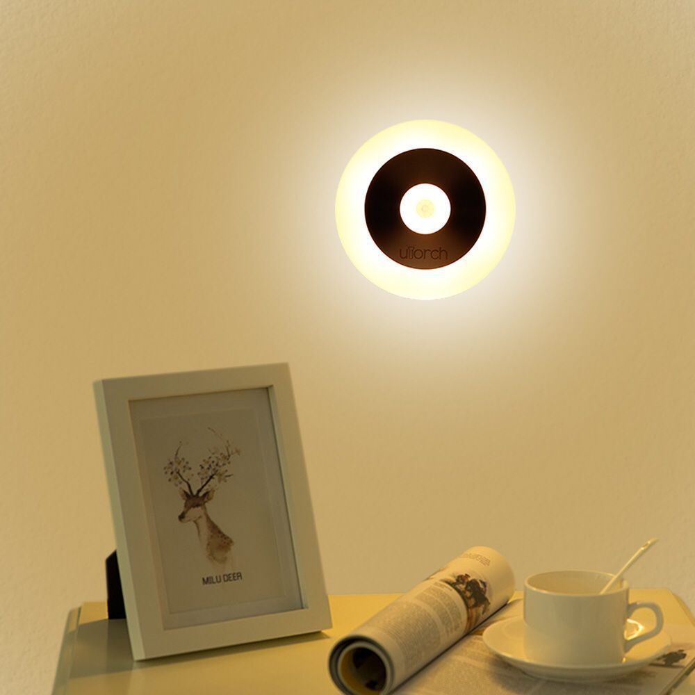 Round night light lit warm above a picture frame and a cup on a shelf
