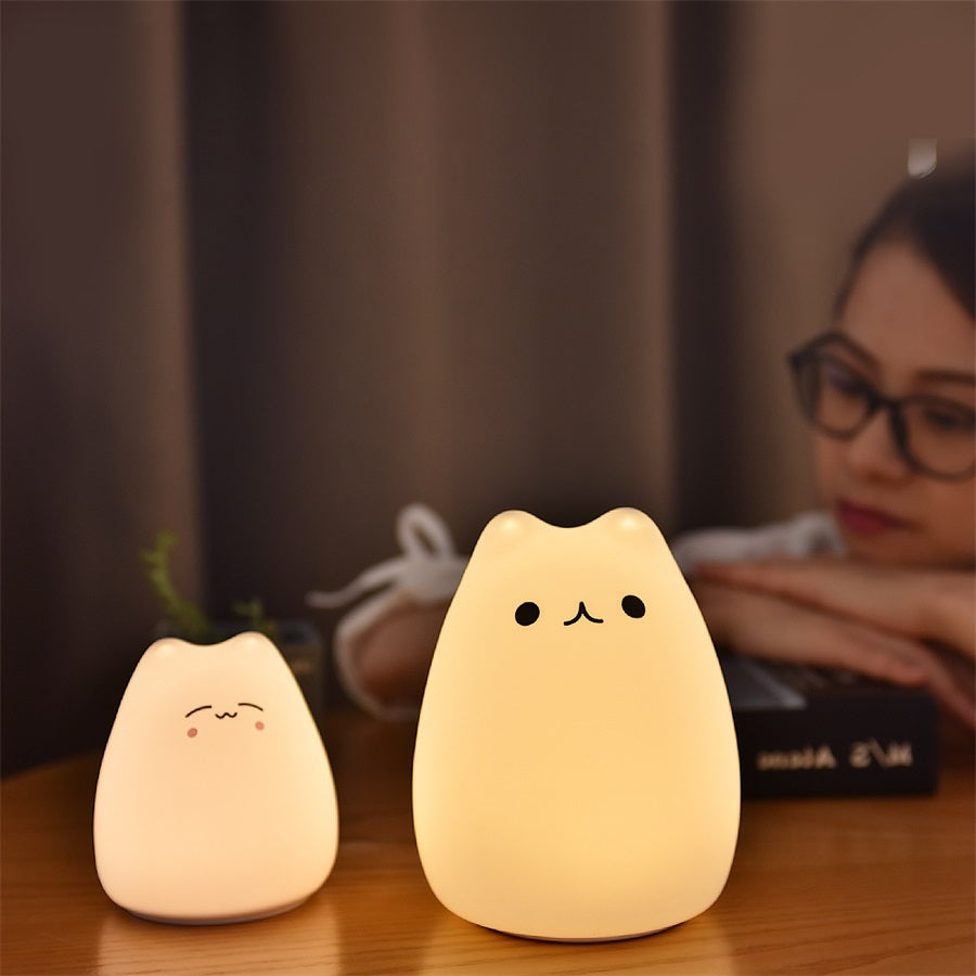 Two silicone cat night lights lit warm on a desk, one small and one large