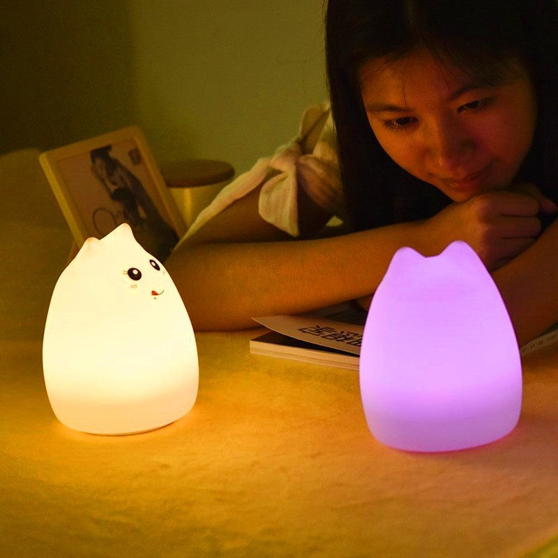 Two silicone cat night lights lit warm and pink beside a person reading