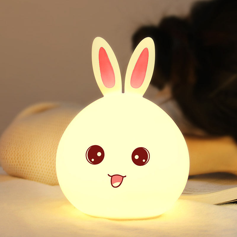 White silicone rabbit night light glowing warm on a bed