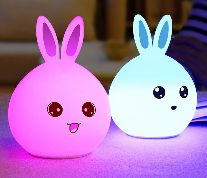 Two silicone rabbit night lights lit pink and blue on a desk