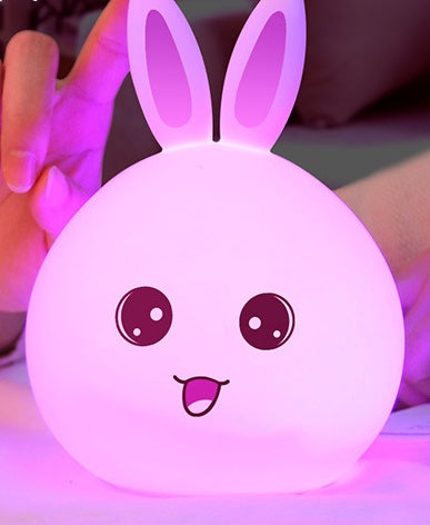 Silicone rabbit night light glowing pink, held from behind