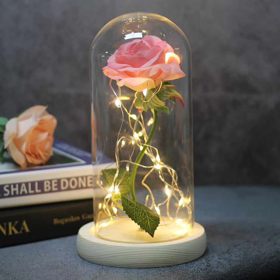 Pink rose in a glass dome with fairy lights on a white base