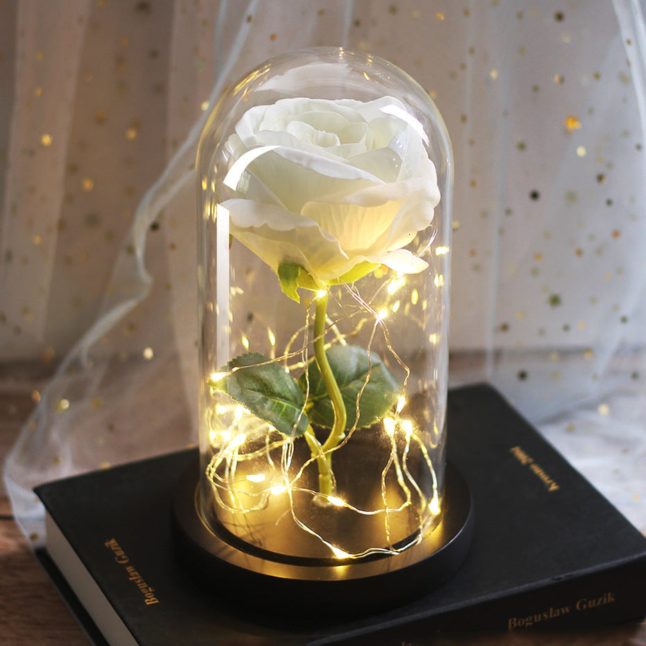 White rose in a glass dome with warm fairy lights, wooden base