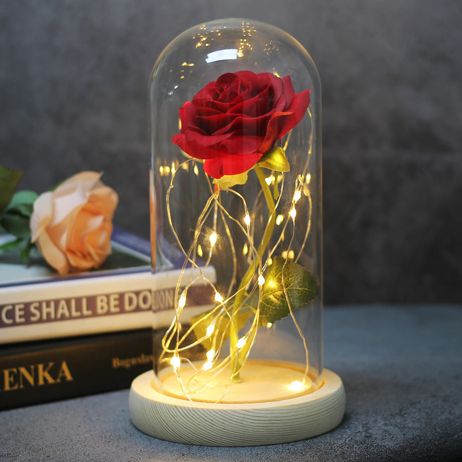 Red rose in a glass dome with fairy lights on a pale wooden base