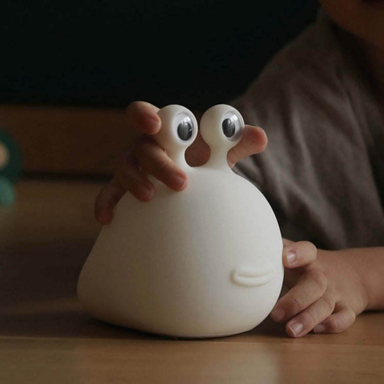 Child touching the white silicone slug night light on a table