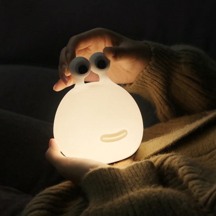 Hand holding the glowing silicone slug night light on a sofa