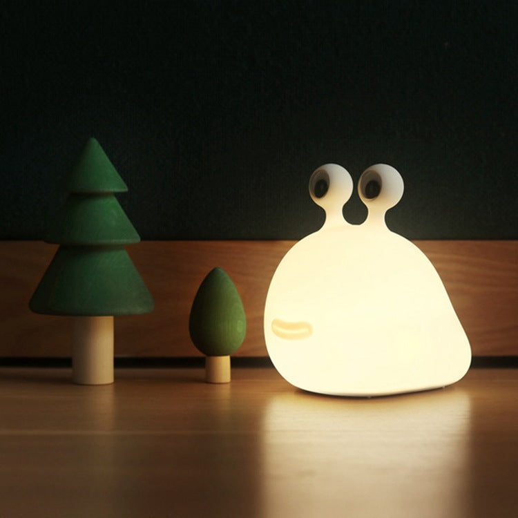 Silicone slug night light glowing beside small wooden trees on a table
