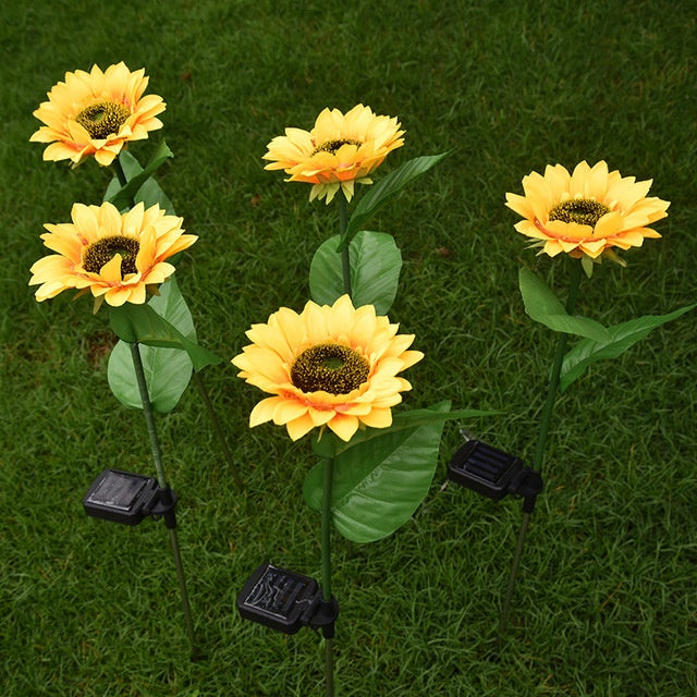 Four sunflower solar lights on stakes pushed into a lawn during the day