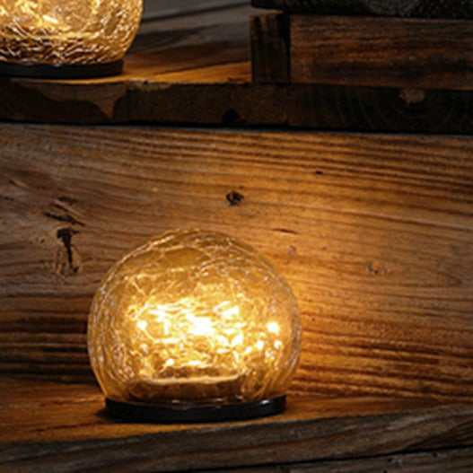 One crackle-glass solar ball light glowing warm on a wooden step