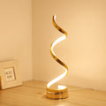 Gold spiral LED table lamp lit warm in a corner beside a picture frame
