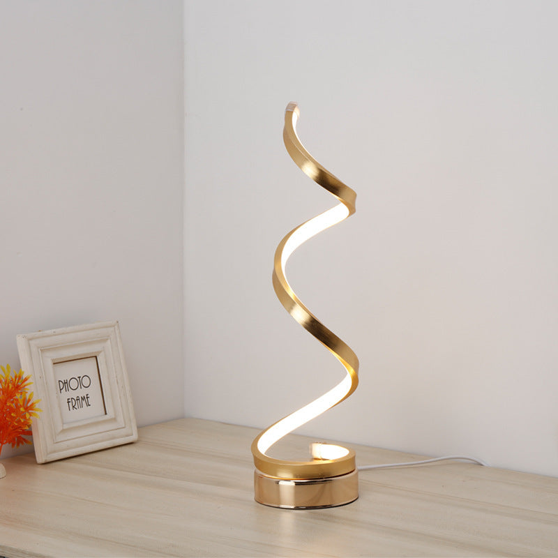 Gold spiral LED table lamp lit warm against a plain wall