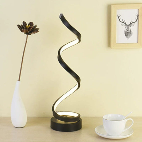 Gold spiral LED lamp lit on a desk beside a vase and a teacup
