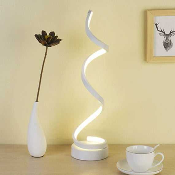 White spiral LED lamp lit on a desk beside a vase and a teacup