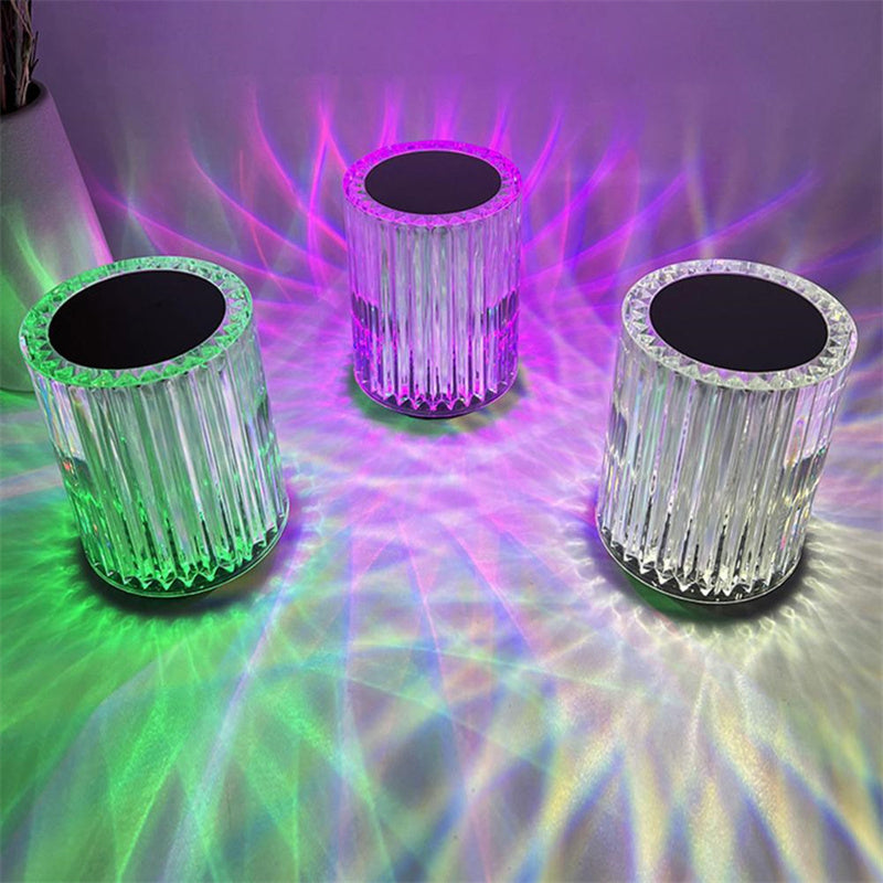 Three ribbed crystal lamps lit green, purple and white on a table