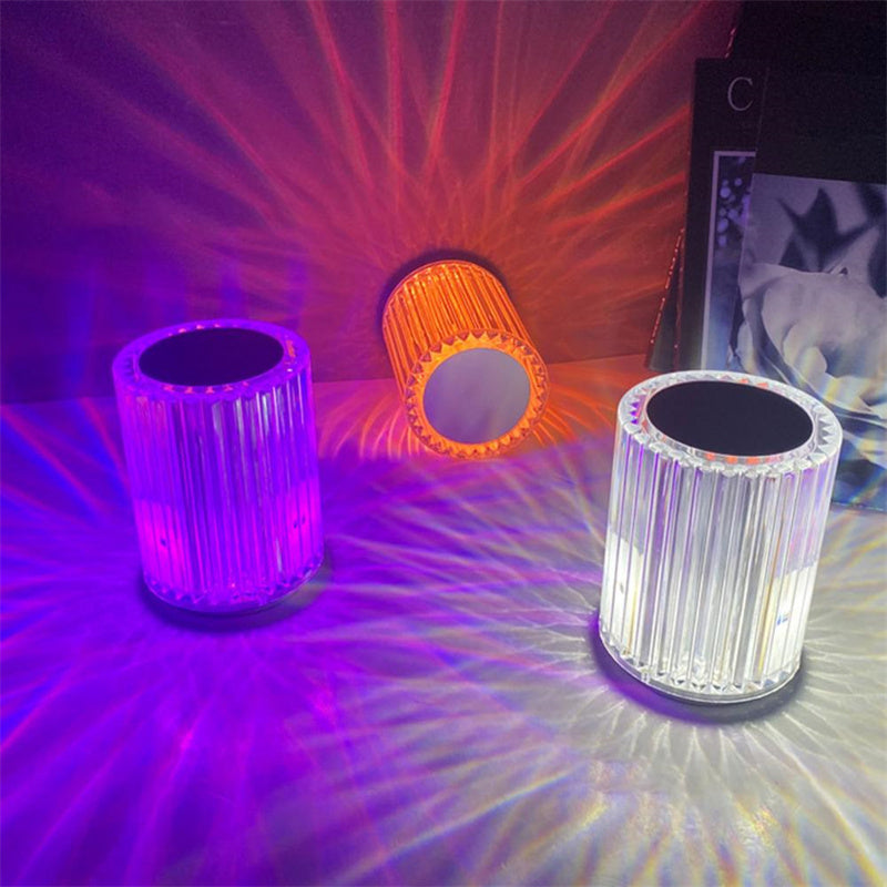 Three ribbed crystal lamps lit purple, orange and white beside a photo frame