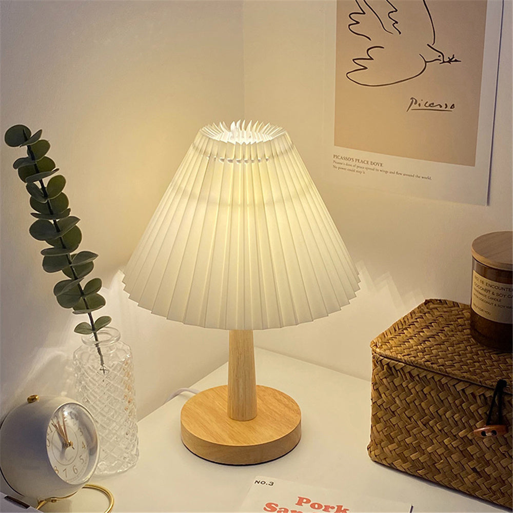 Pleated-shade table lamp lit on a desk beside eucalyptus stems and a basket