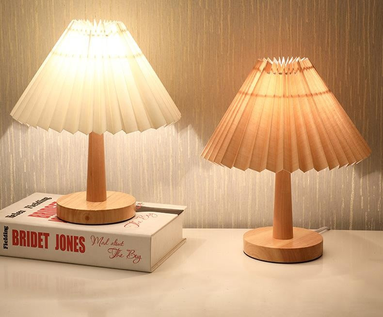 Cream and beige pleated table lamps lit side by side on a white surface