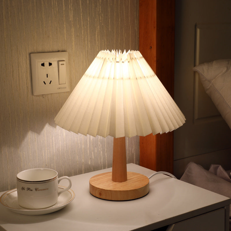 Pleated-shade table lamp lit on a nightstand beside a teacup